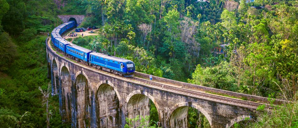 A blue train crosses the iconic Nine Arch Bridge in Ella, surrounded by lush green Sri Lankan jungle.