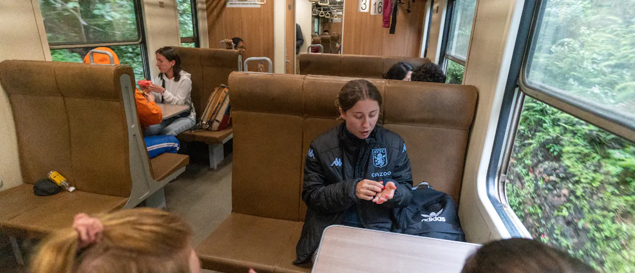 Two women relax inside a train, passing lush green scenery on a journey through Sri Lanka.
