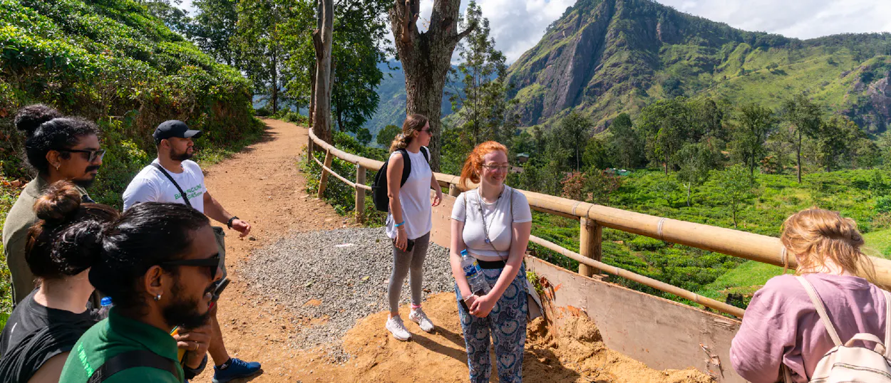 A group of smiling travelers on a mountain path, enjoying views of lush tea plantations in Ella.