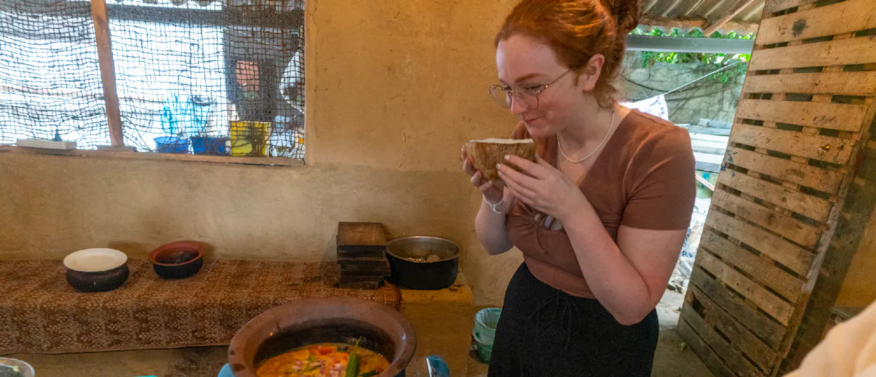 A woman smells a drink in a coconut shell during a cooking class in Ella, Sri Lanka.