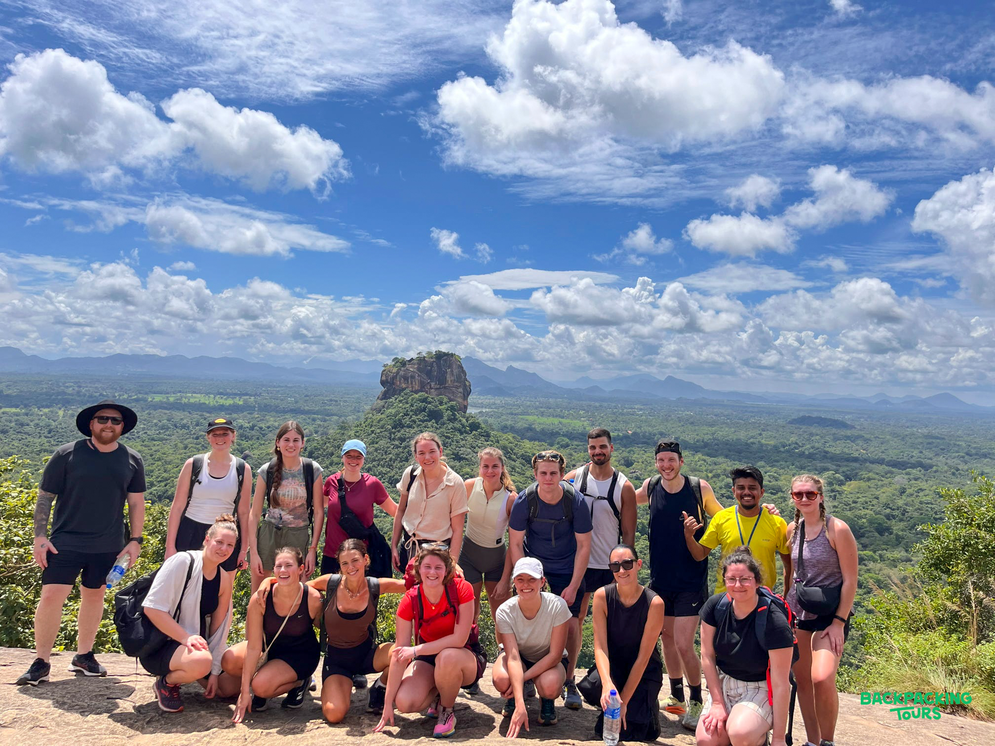 Happy backpackers pose on a rocky outcrop, enjoying panoramic views of Sigiriya in Sri Lanka.