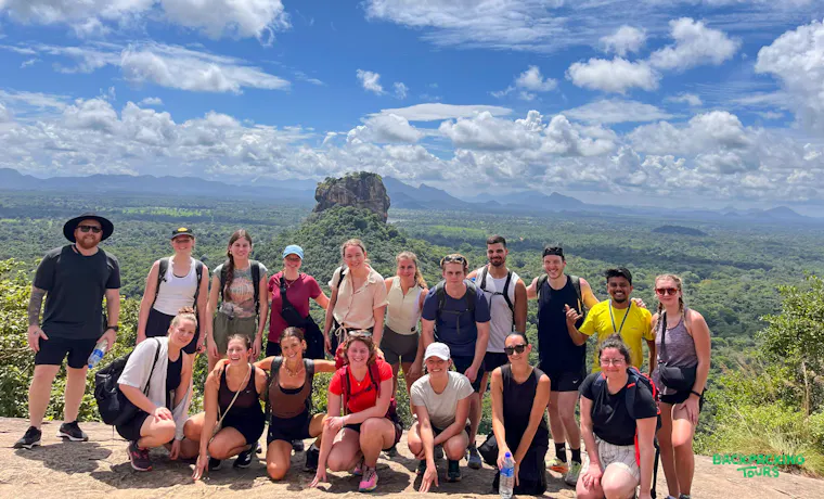 Happy backpackers pose on a rocky outcrop, enjoying panoramic views of Sigiriya in Sri Lanka.