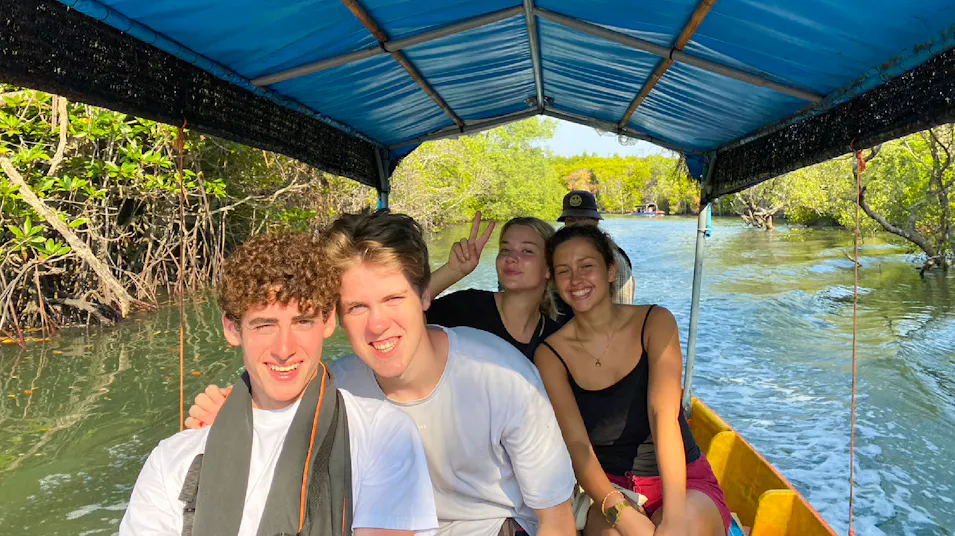 Four happy young people enjoy a longtail boat ride through a lush mangrove forest in Thailand.