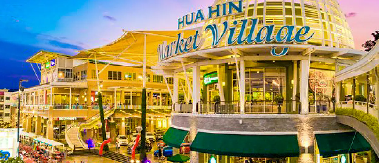 Hua Hin Market Village, a vibrant multi-story shopping complex, illuminated at dusk with warm lights.