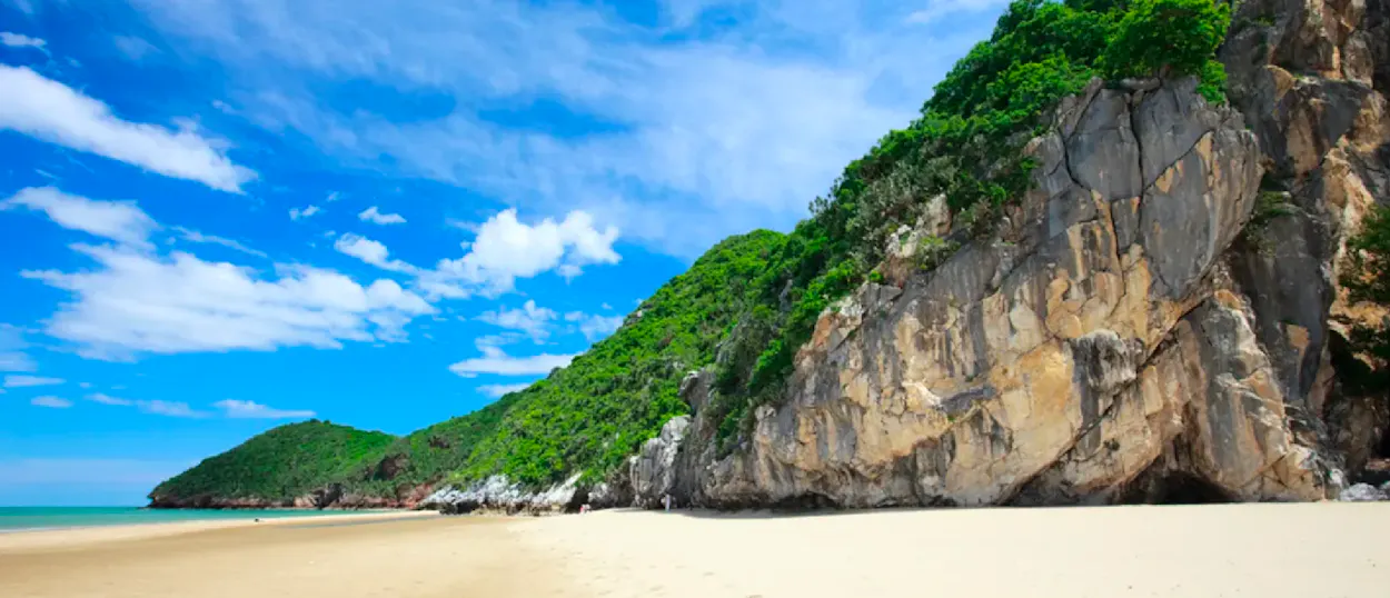 Idyllic Khao Kalok Beach with a vast sandy expanse, towering green cliffs, and clear blue water.