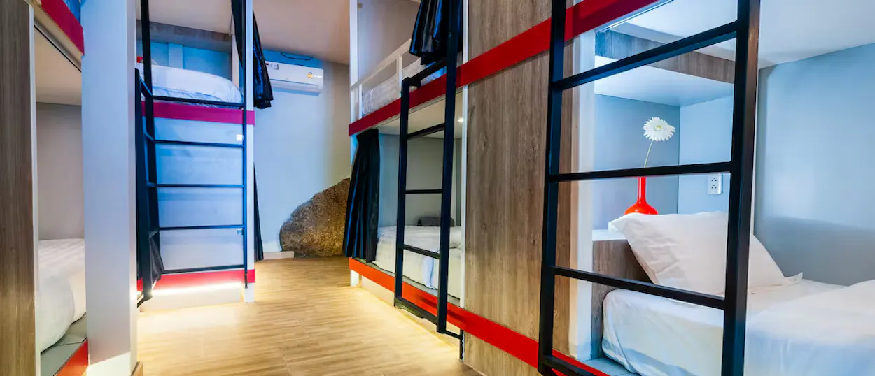 Bright and clean hostel dormitory room featuring modern bunk beds with privacy curtains and red details.