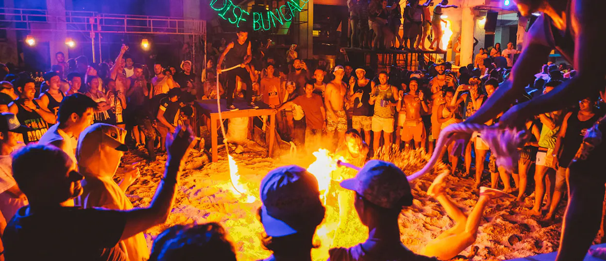 Excited crowd watches a person jump a flaming skipping rope at the lively Full Moon Party.
