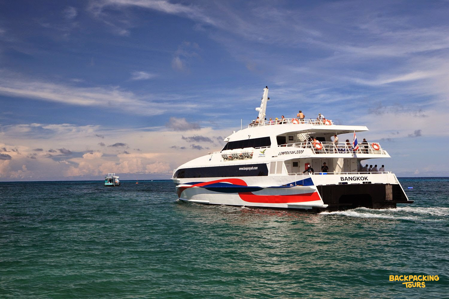 A large ferry carries passengers across the clear blue sea, departing Koh Phangan under a sunny sky.