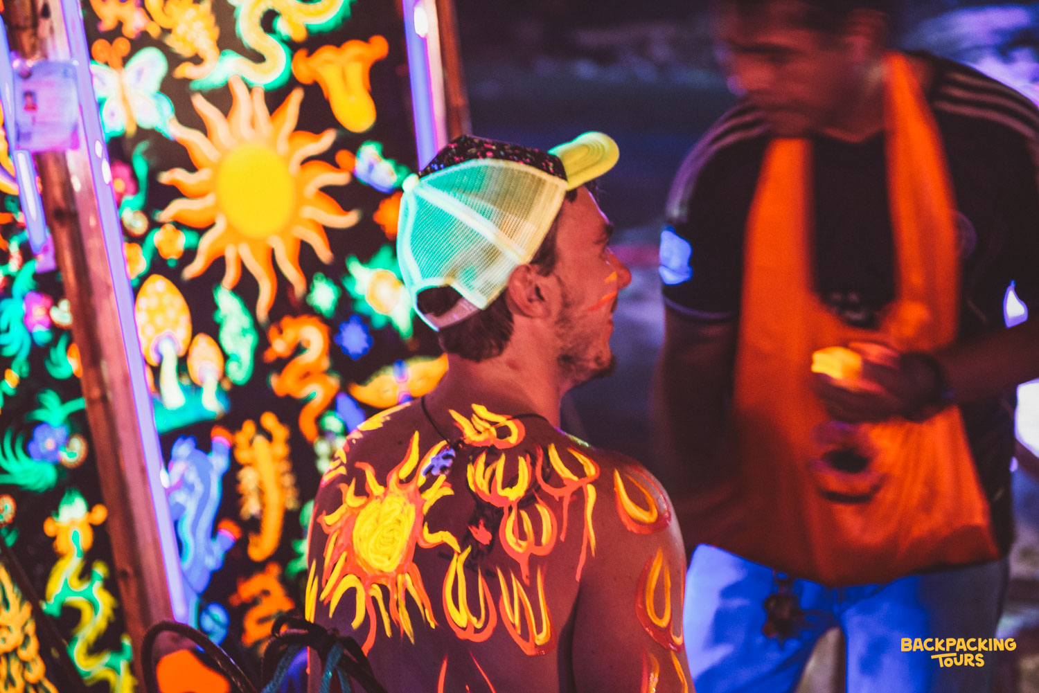 A man's back painted with glowing neon suns at the lively Full Moon Party on Koh Phangan.