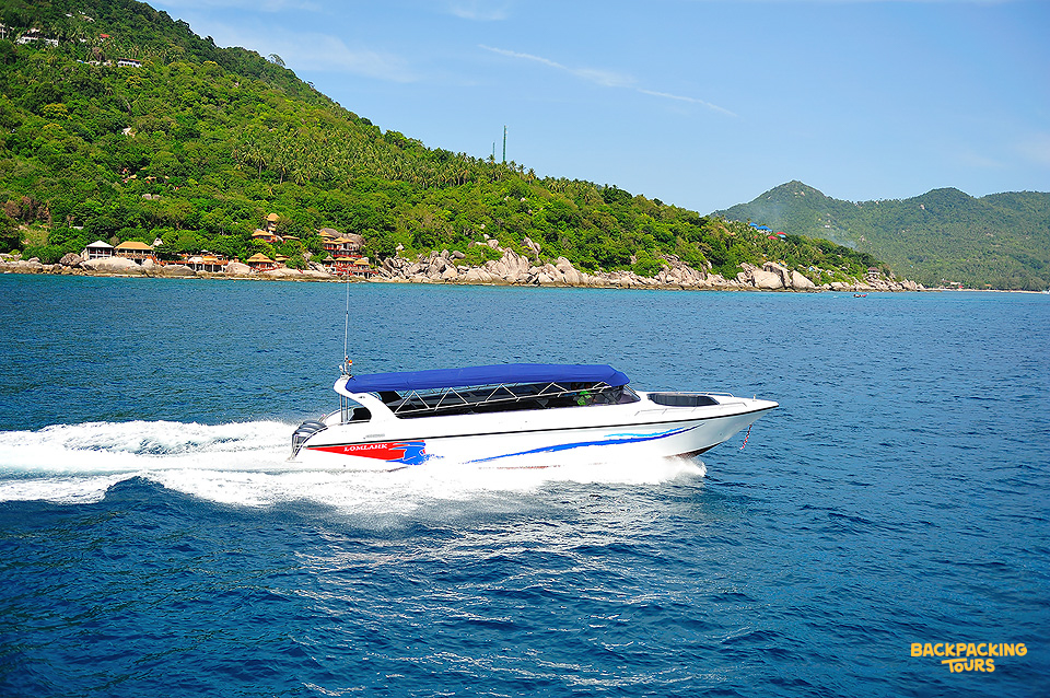 A white speed boat cruises across the clear blue waters of Koh Tao, passing a lush green island.