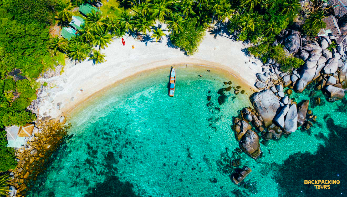Tropical beach on Koh Phangan with white sand, turquoise water, palm trees, and a longtail boat.