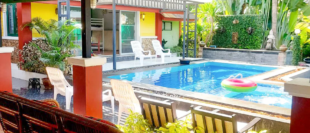 A colorful guesthouse with a bright blue swimming pool, lounge chairs, and lush tropical plants.