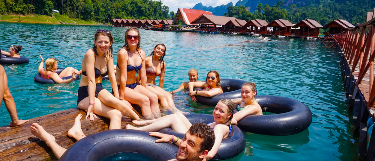 Smiling travelers enjoy swimming and relaxing in inner tubes at Khao Sok's floating bungalows.