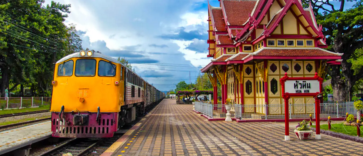 A yellow train waits at the beautifully ornate Hua Hin railway station in Thailand.