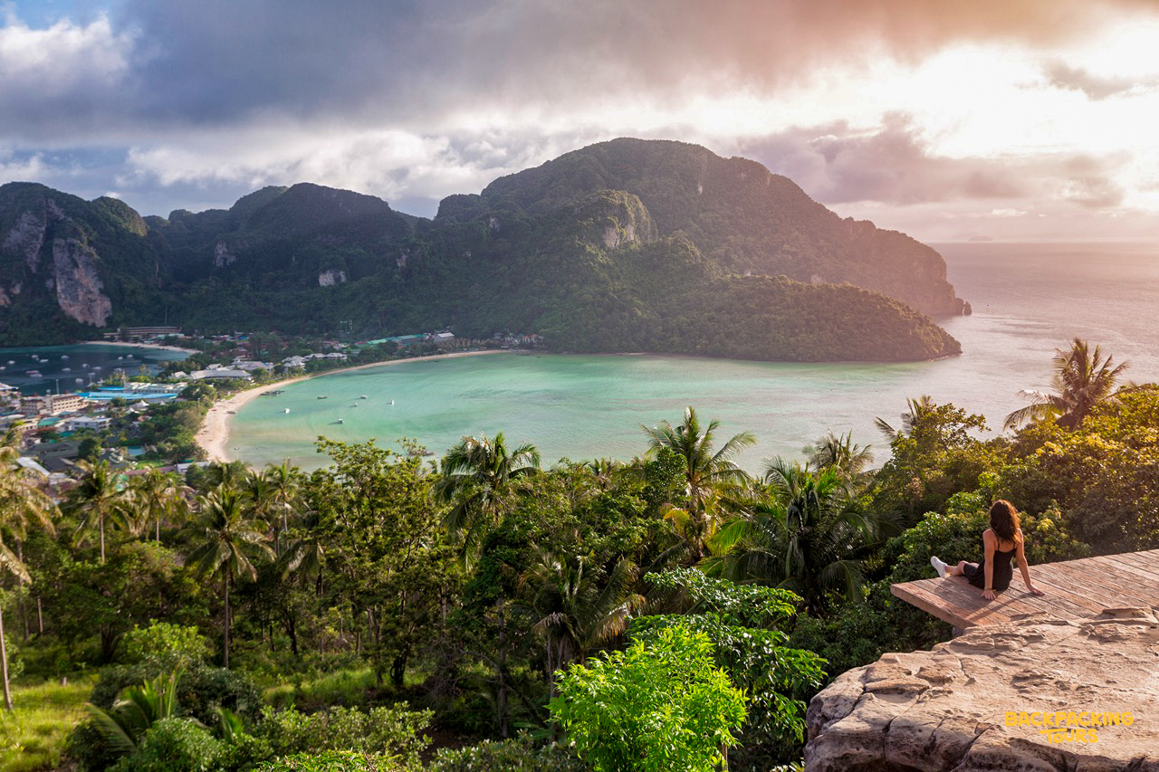 A woman sits on a viewpoint overlooking the beautiful turquoise bay of Phi Phi Islands at sunrise.