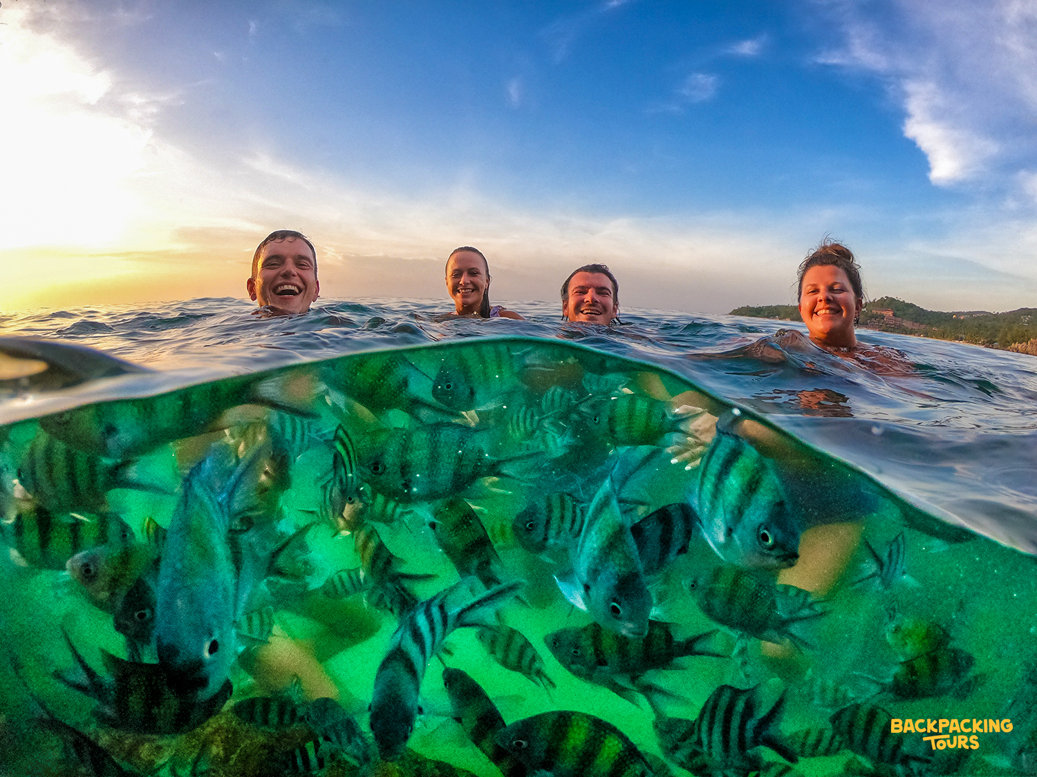 Smiling friends enjoy swimming with vibrant striped fish in the clear green waters off Koh Phangan.