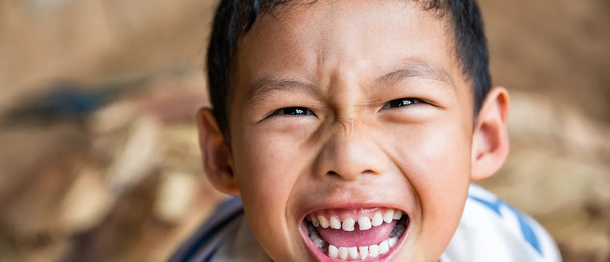 A young boy from a hill tribe community in Chiang Mai smiles joyfully at the camera.