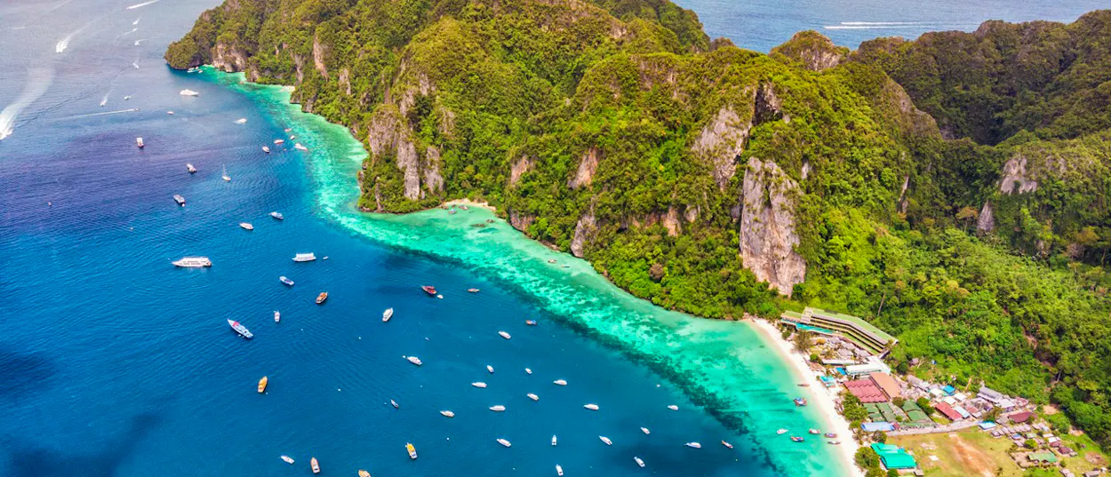 Many boats dot the vibrant turquoise waters along the lush green cliffs of Phi Phi Islands.