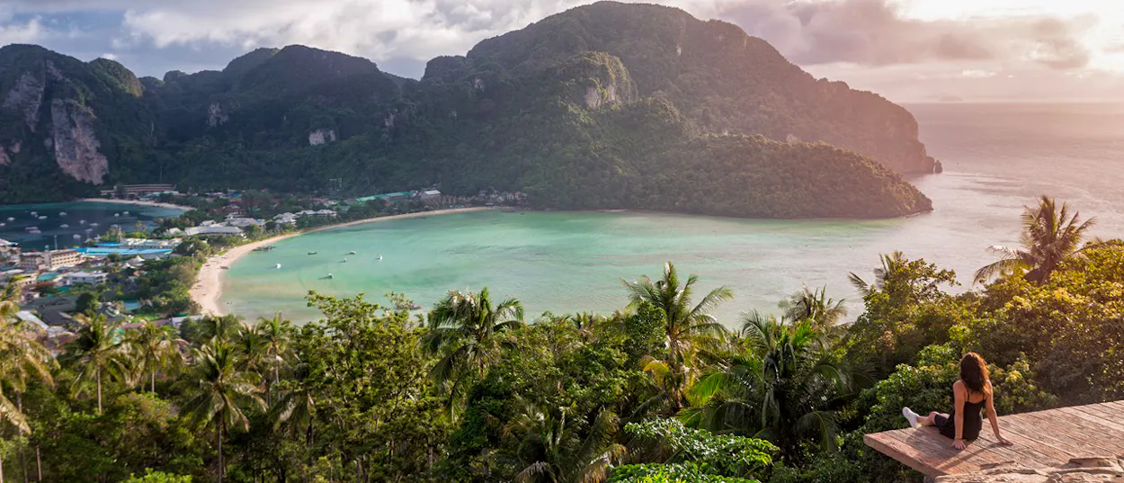 Woman watches a stunning sunrise over Phi Phi Islands bay with lush green mountains.