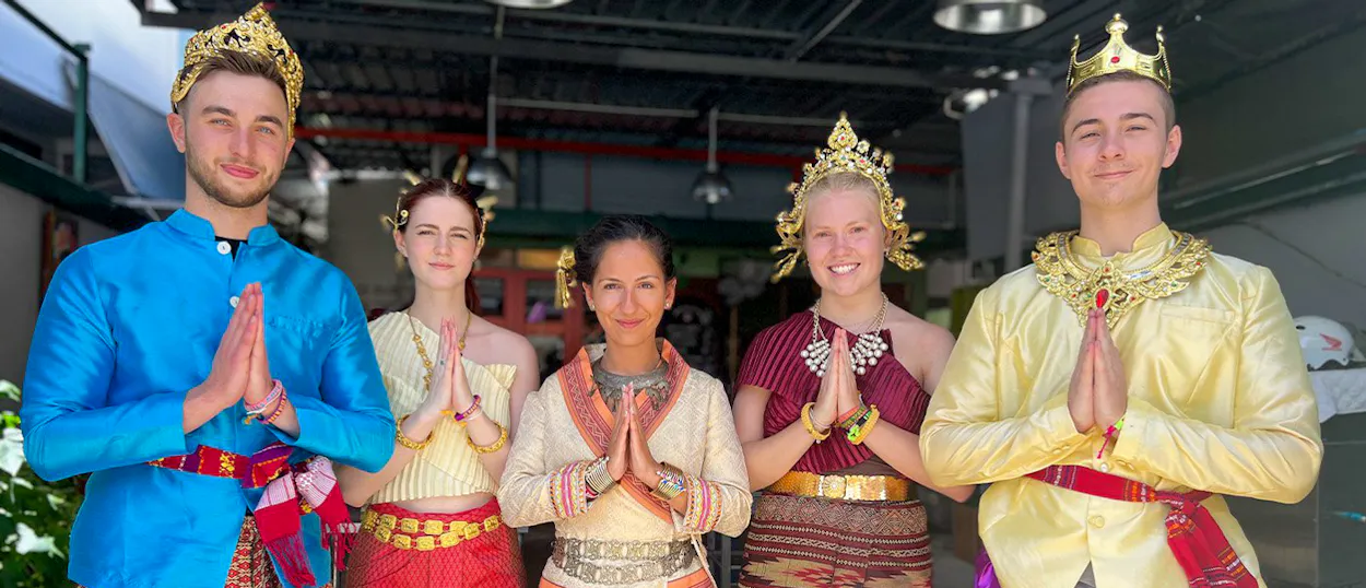 Five people in colorful traditional Thai costumes perform a respectful wai greeting in Bangkok.