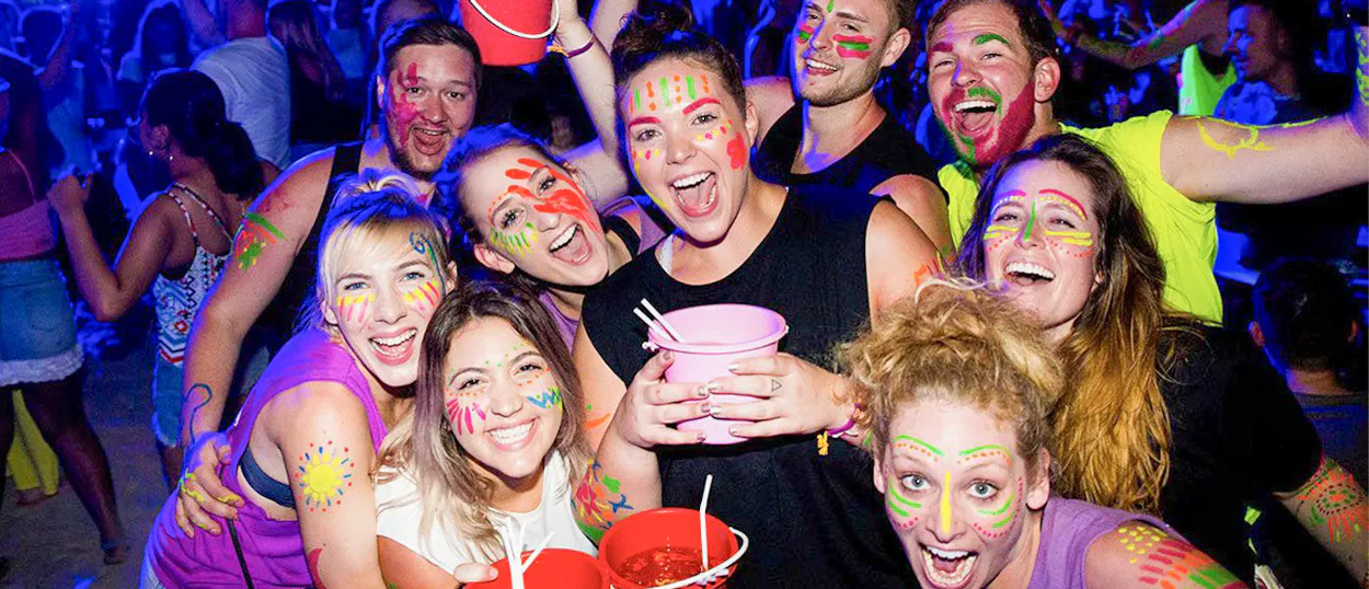 A group of happy friends with glow paint on their faces and bodies at a lively night party.