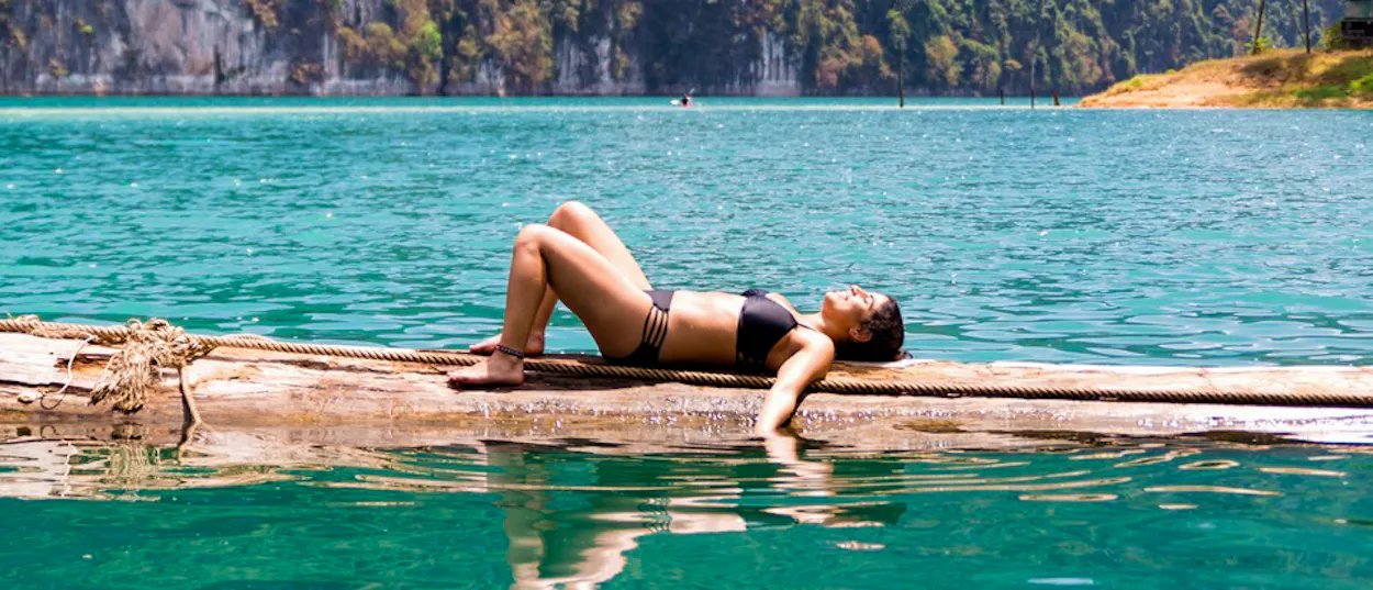A woman relaxes on a floating log in the clear turquoise waters of Khao Sok lake.
