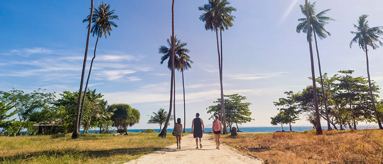 Three people walk along a sandy path towards the turquoise ocean on Thailand's Phi Phi Islands.