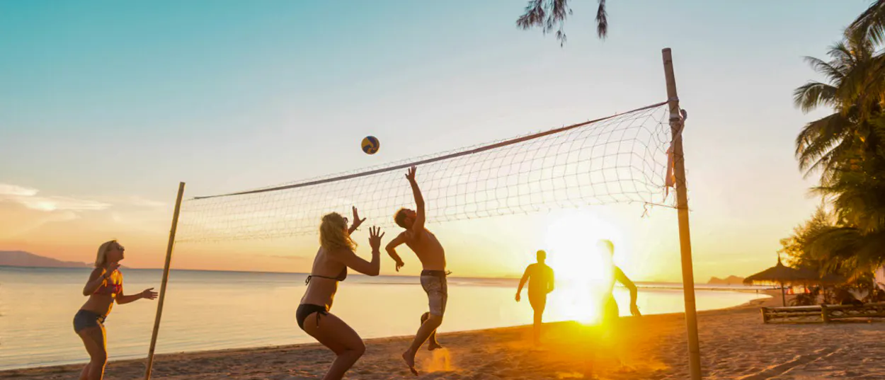 Friends playing beach volleyball on a sandy shore during a vibrant sunset in Koh Phangan, Thailand.