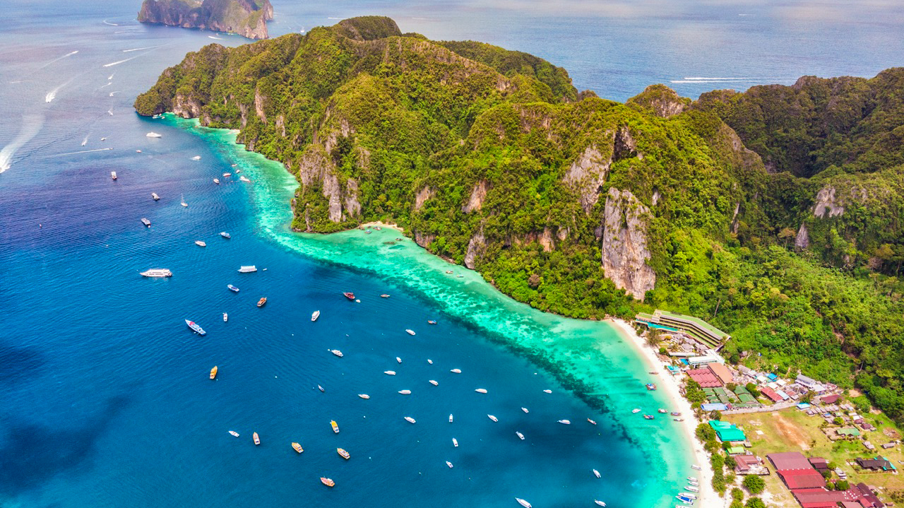 Aerial view of Phi Phi Islands, Thailand, with boats in clear turquoise water and green cliffs.