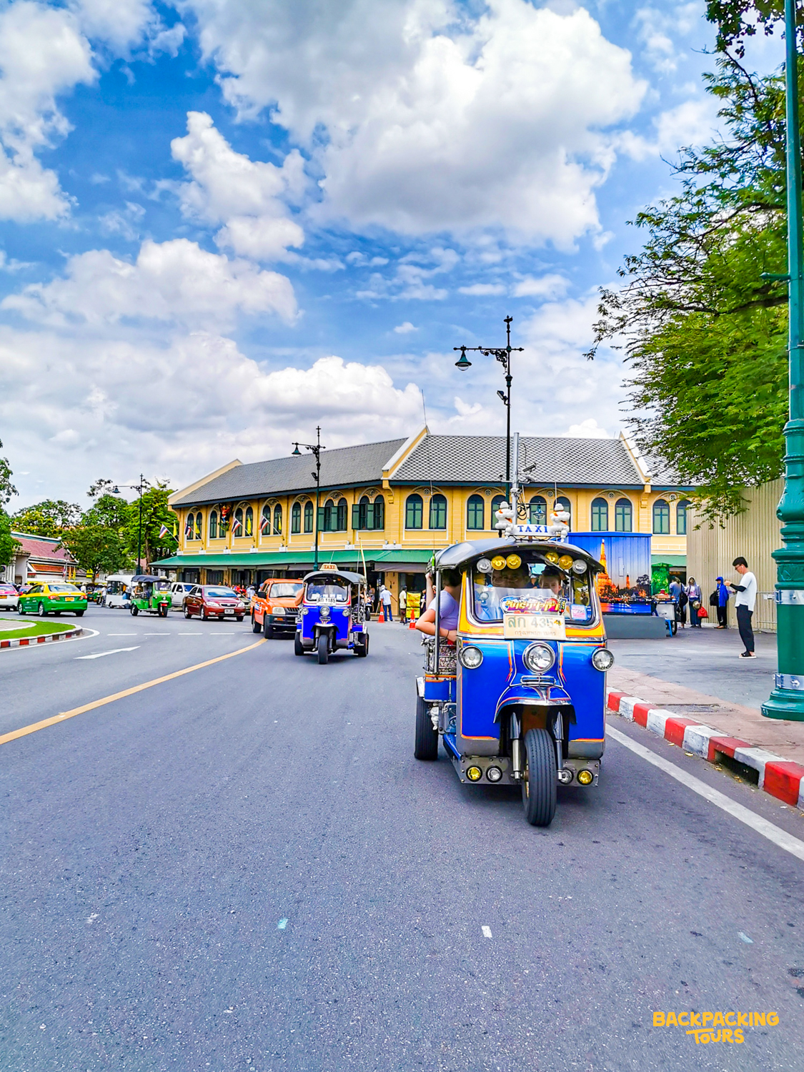 Riding a blue and yellow tuk-tuk through the lively streets of Bangkok on a sunny day.