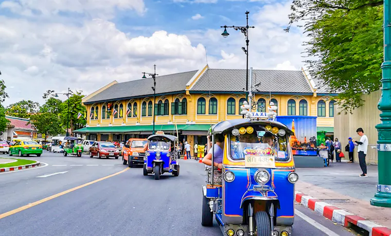 Riding a blue and yellow tuk-tuk through the lively streets of Bangkok on a sunny day.