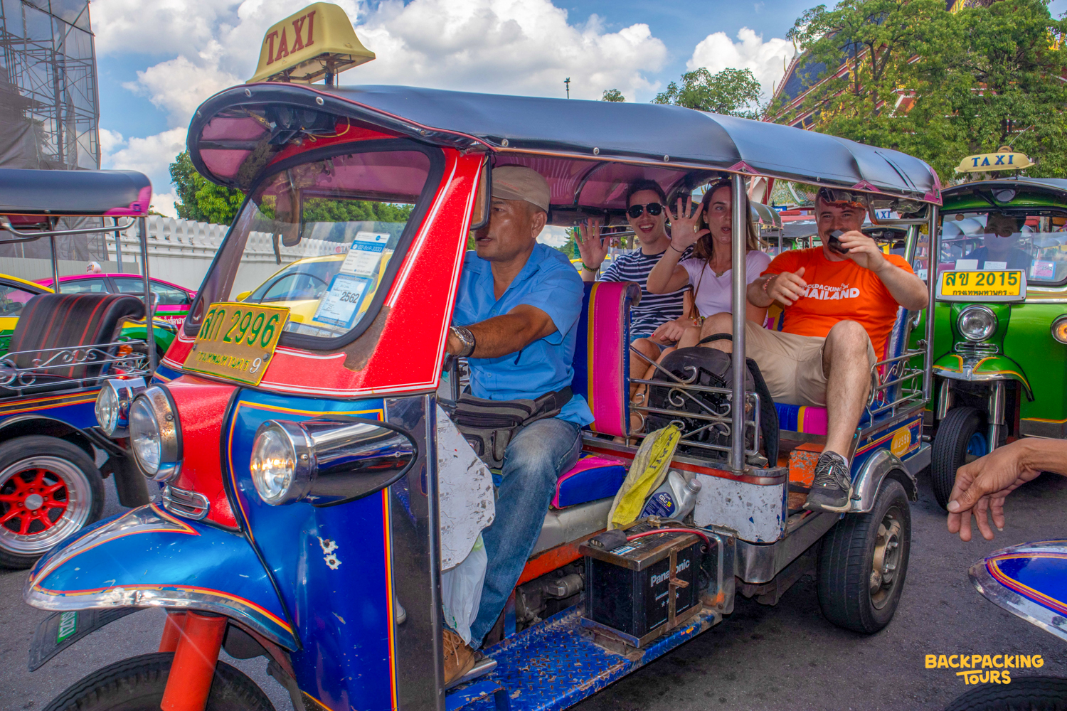 Happy travelers wave from a colorful tuk-tuk, exploring the bustling streets of Bangkok.