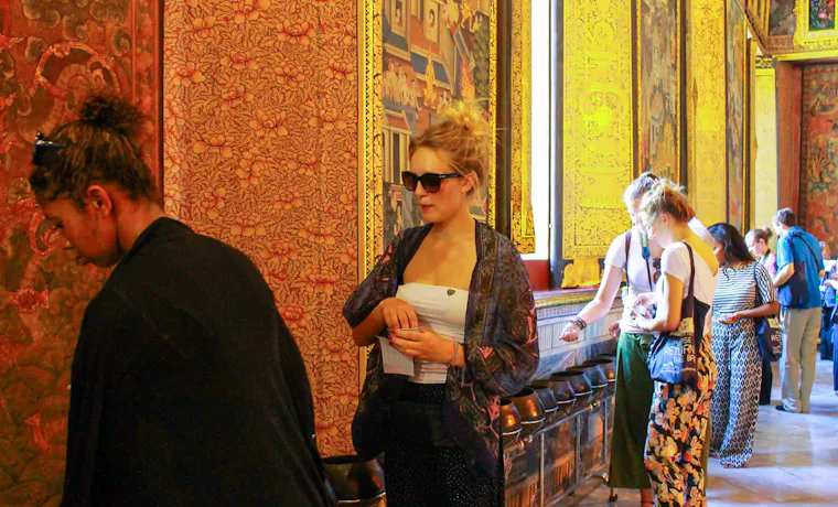 Travelers observing the ornate wall paintings and architecture within a Thai temple in Bangkok.