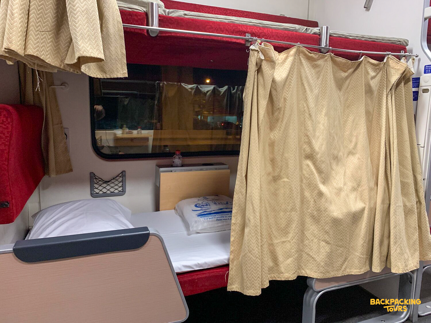 Comfortable sleeper train cabin in Thailand with a made-up lower bunk and privacy curtains.