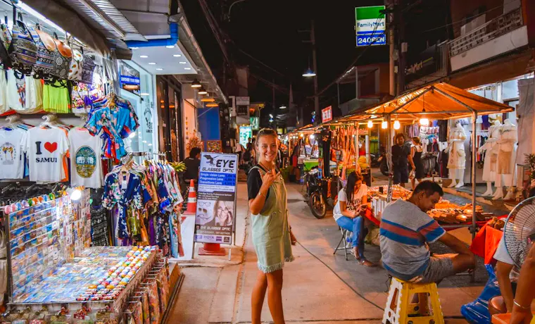 Smiling woman gives a thumbs-up at a bustling night market in Fisherman's Village, Koh Samui.