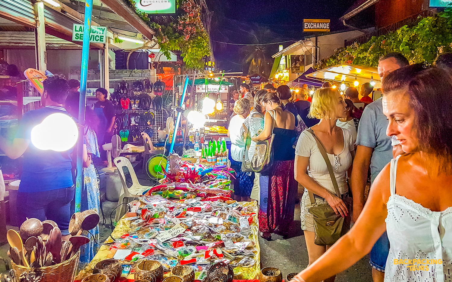 Visitors explore a lively night market in Koh Samui, shopping for unique souvenirs and local goods.