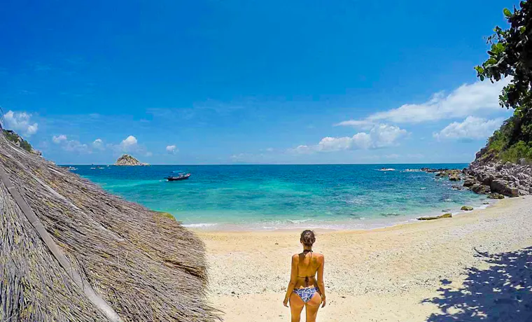 A woman in a bikini walks towards the clear blue ocean on a sandy beach in Koh Tao.