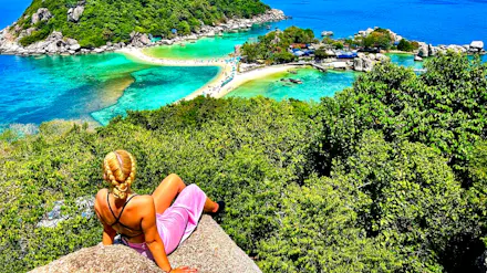 Blonde woman on a rock gazes at the stunning turquoise sea and connecting sandbar of Koh Nangyuan.