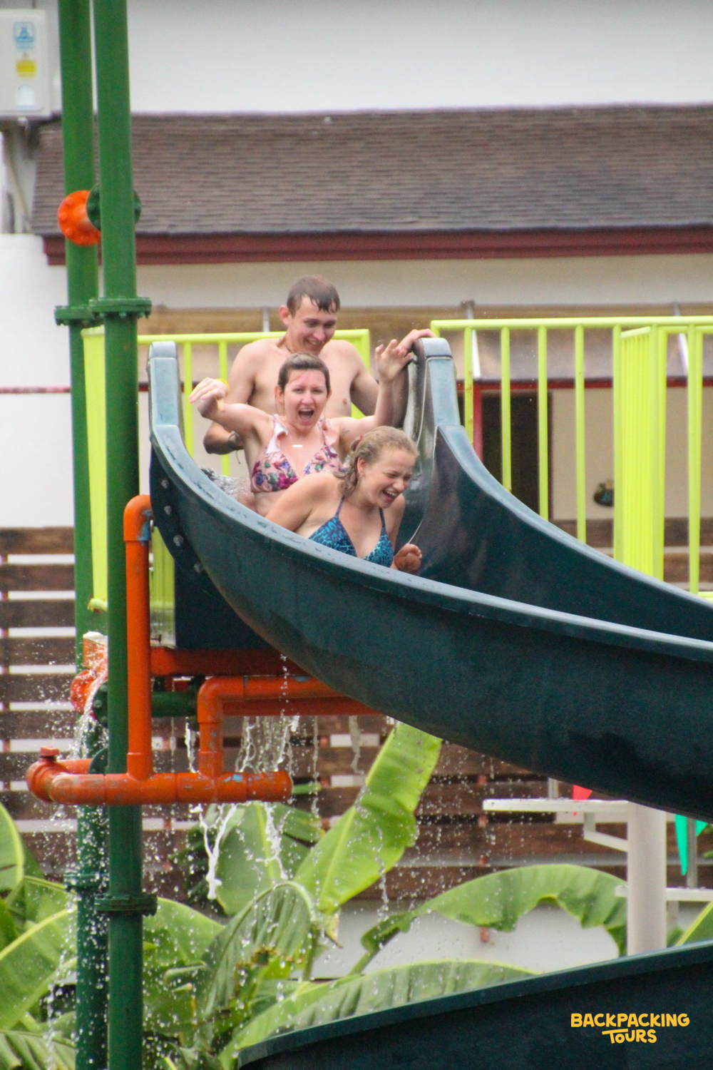 Three friends laughing and splashing down a water slide at a resort in Krabi, Thailand.