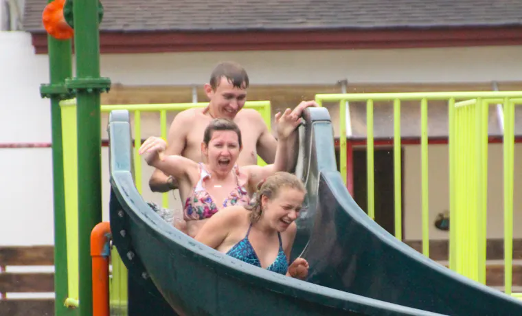 Three friends laughing and splashing down a water slide at a resort in Krabi, Thailand.