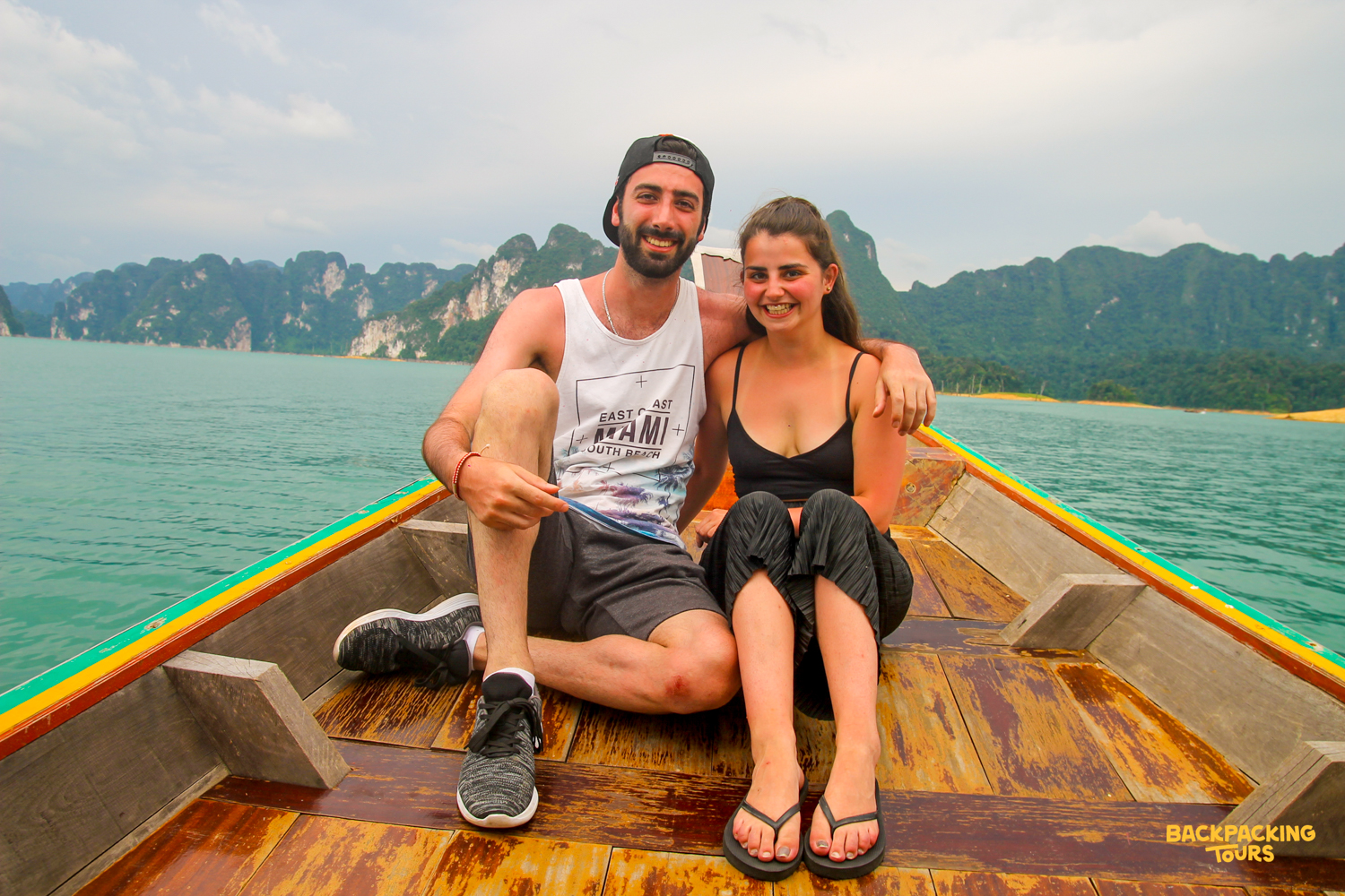 Two smiling travelers on a longtail boat, exploring the stunning Khao Sok National Park.