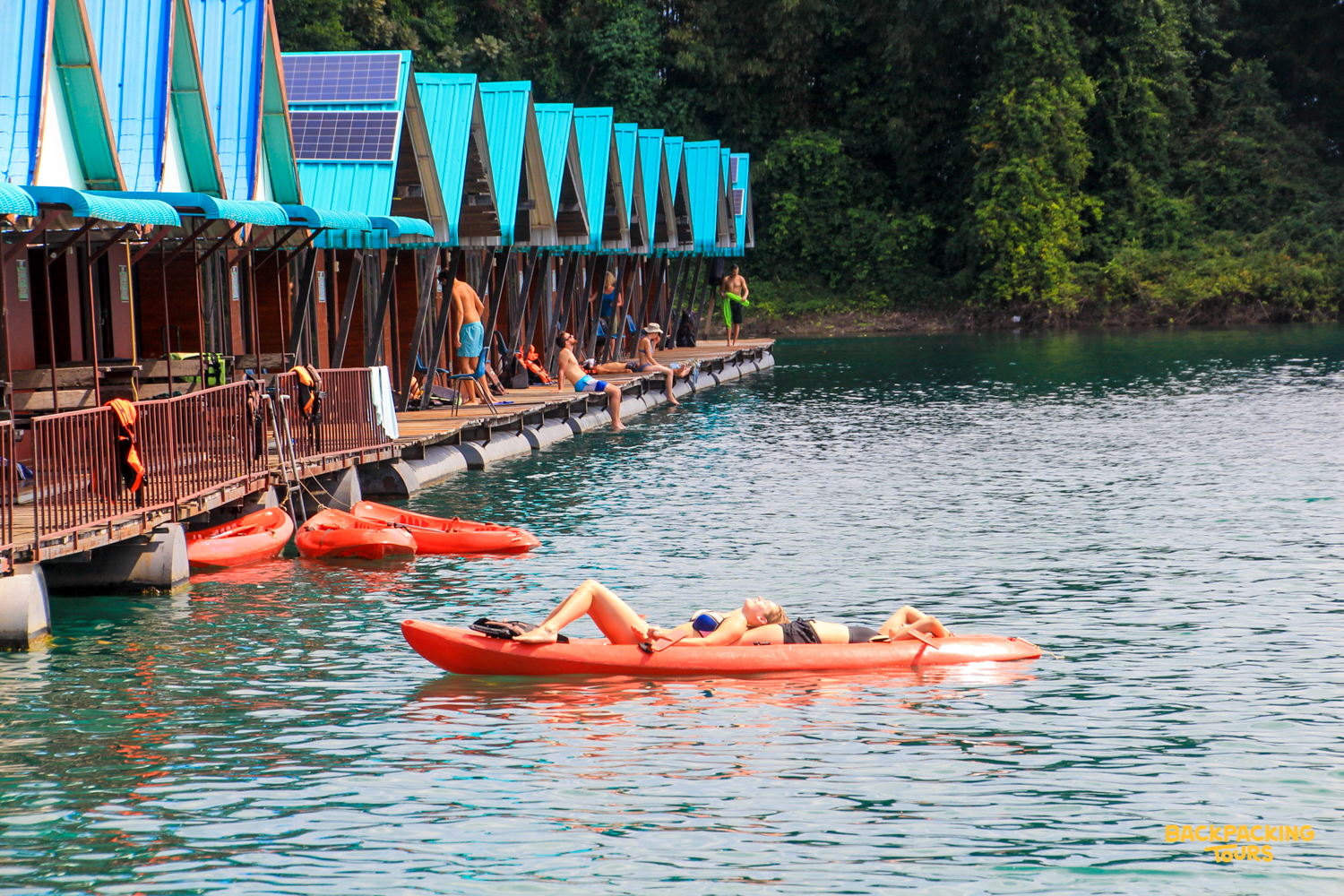 Travelers relax on floating bungalows and kayaks on the clear waters of Cheow Lan Lake.
