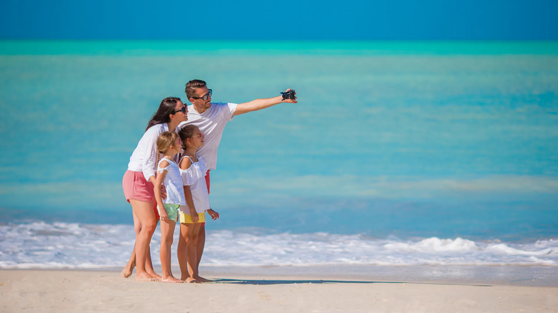 A happy family takes a selfie on a beautiful white sand beach with turquoise water in Thailand.