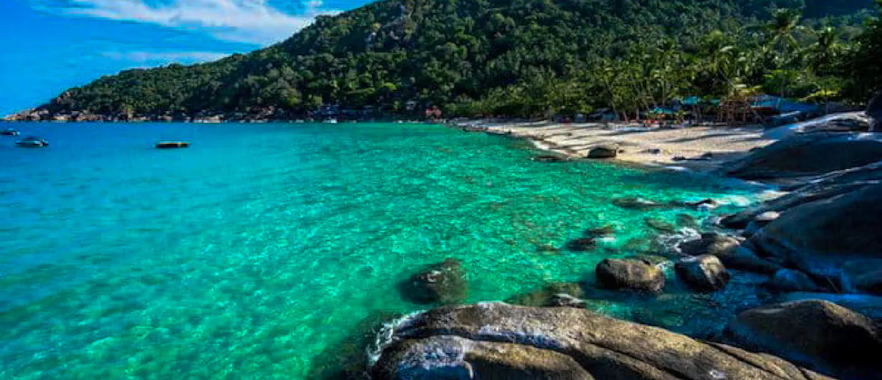 Beautiful tropical beach with clear turquoise water, sandy shore, and lush green hills on Koh Phangan.