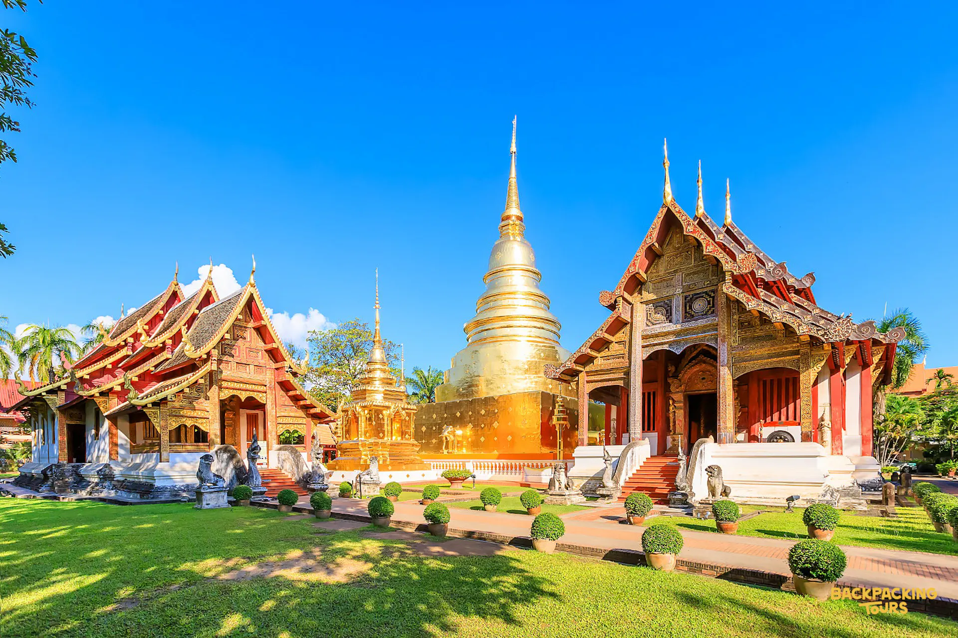 Magnificent golden Thai temples and stupas with ornate roofs and spires under a bright blue sky.