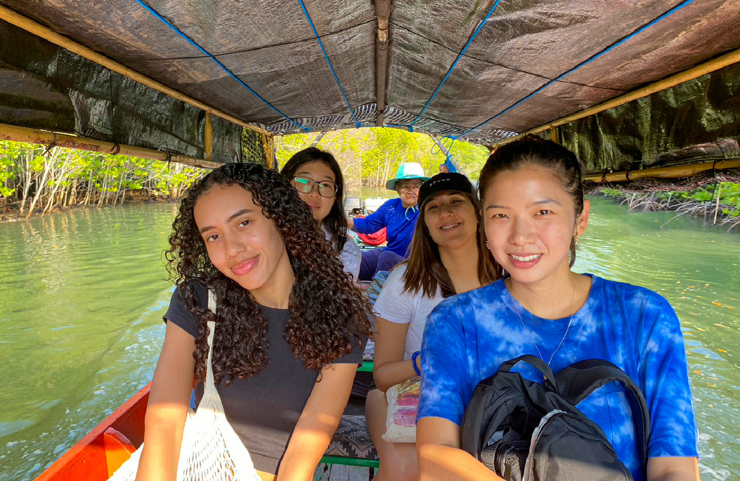 Smiling young women enjoy a scenic longtail boat ride through lush mangroves in Thailand.