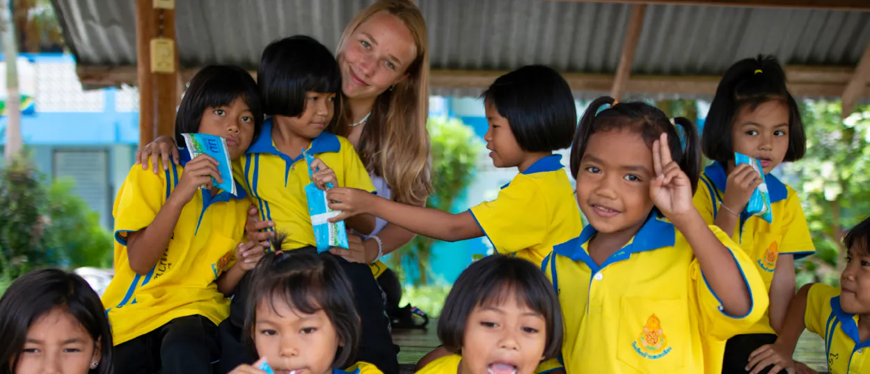 A smiling volunteer poses with cheerful Thai students in yellow uniforms during a school break.