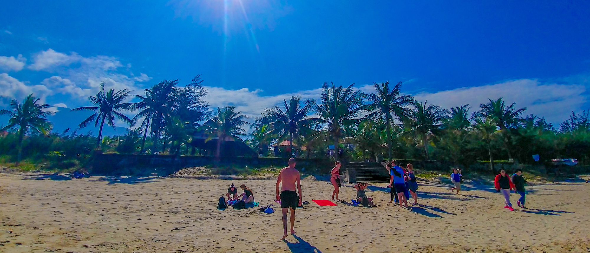 Travelers relax and socialize on a sunny sandy beach lined with palm trees in Nha Trang, Vietnam.