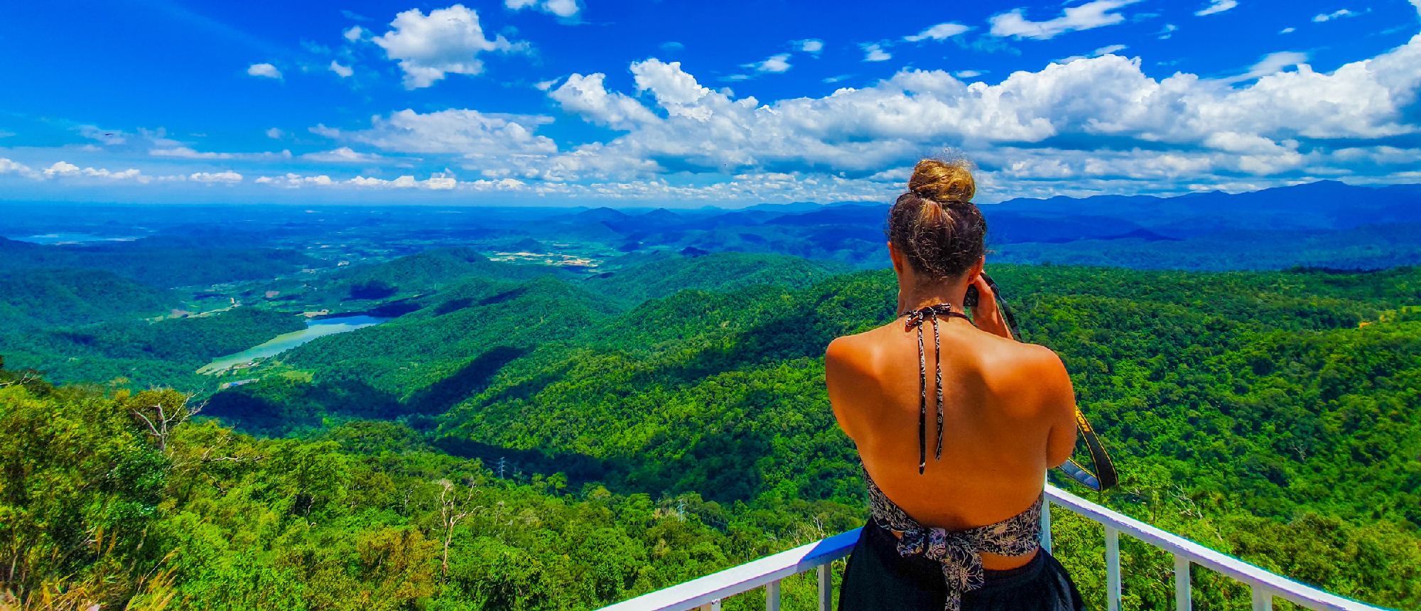 Traveler gazes at the expansive forested landscape and distant lake under a bright blue sky in Vietnam.