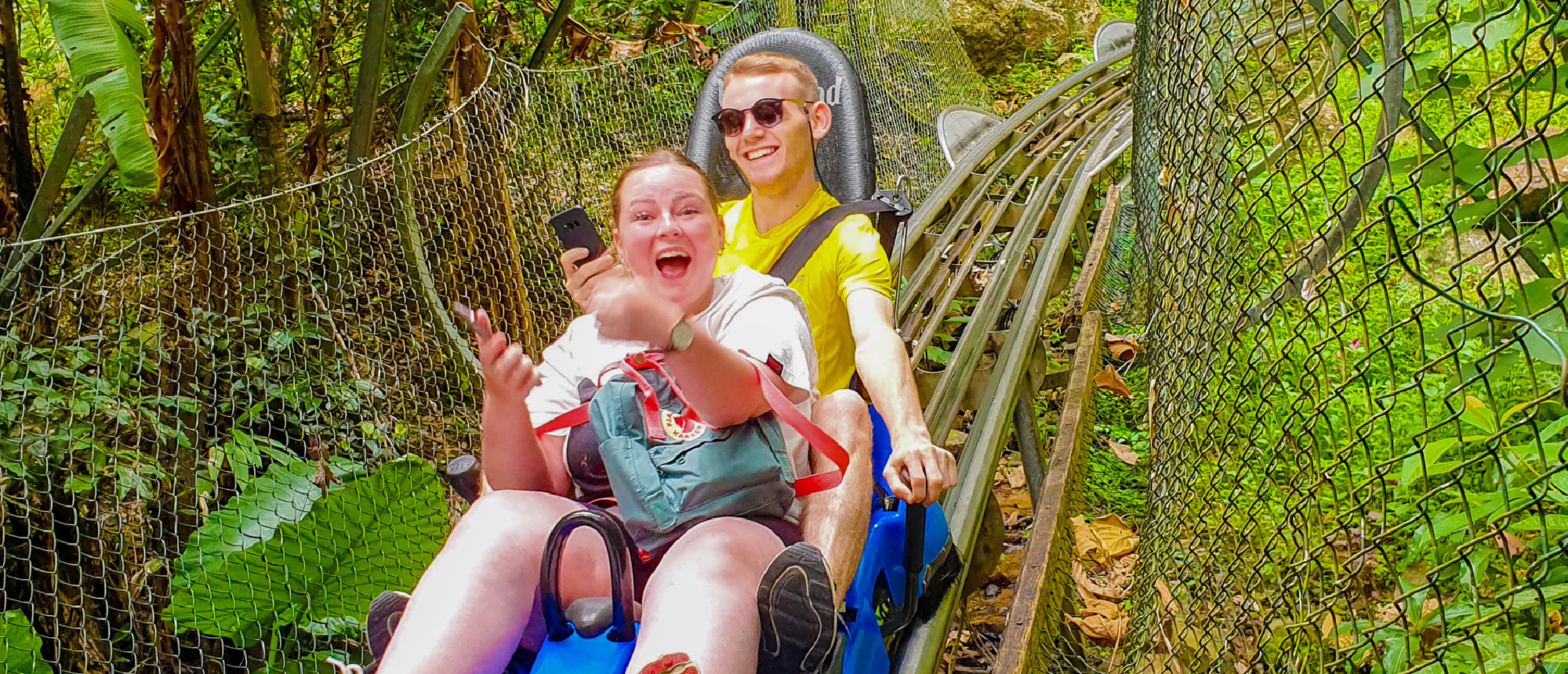 Two excited travelers riding an alpine coaster through lush green jungle at Datanla Waterfalls.